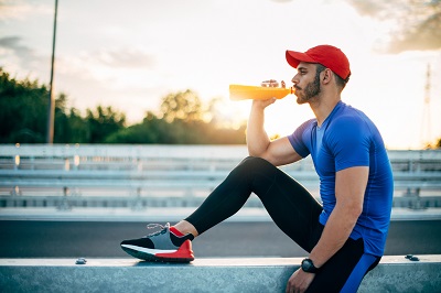 Man in running clothes drinking orange sports drink with vitamin C