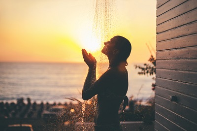 Woman detoxing with glutathione in outdoor shower near beach at sunset